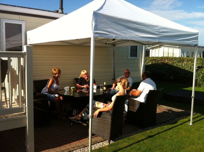 A white 3m Pop Up Gazebo being used as a patio shelter besides a static caravan