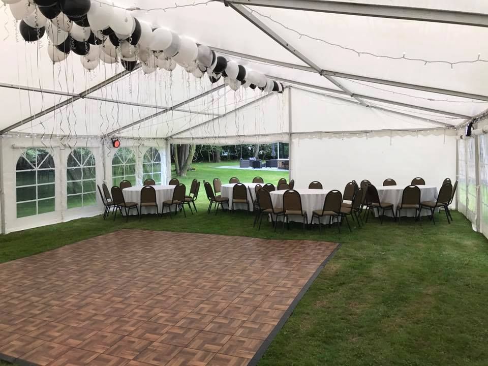 An interior view of a marquee decorated for a party with balloons, a portable dance floor, lined tables and chairs