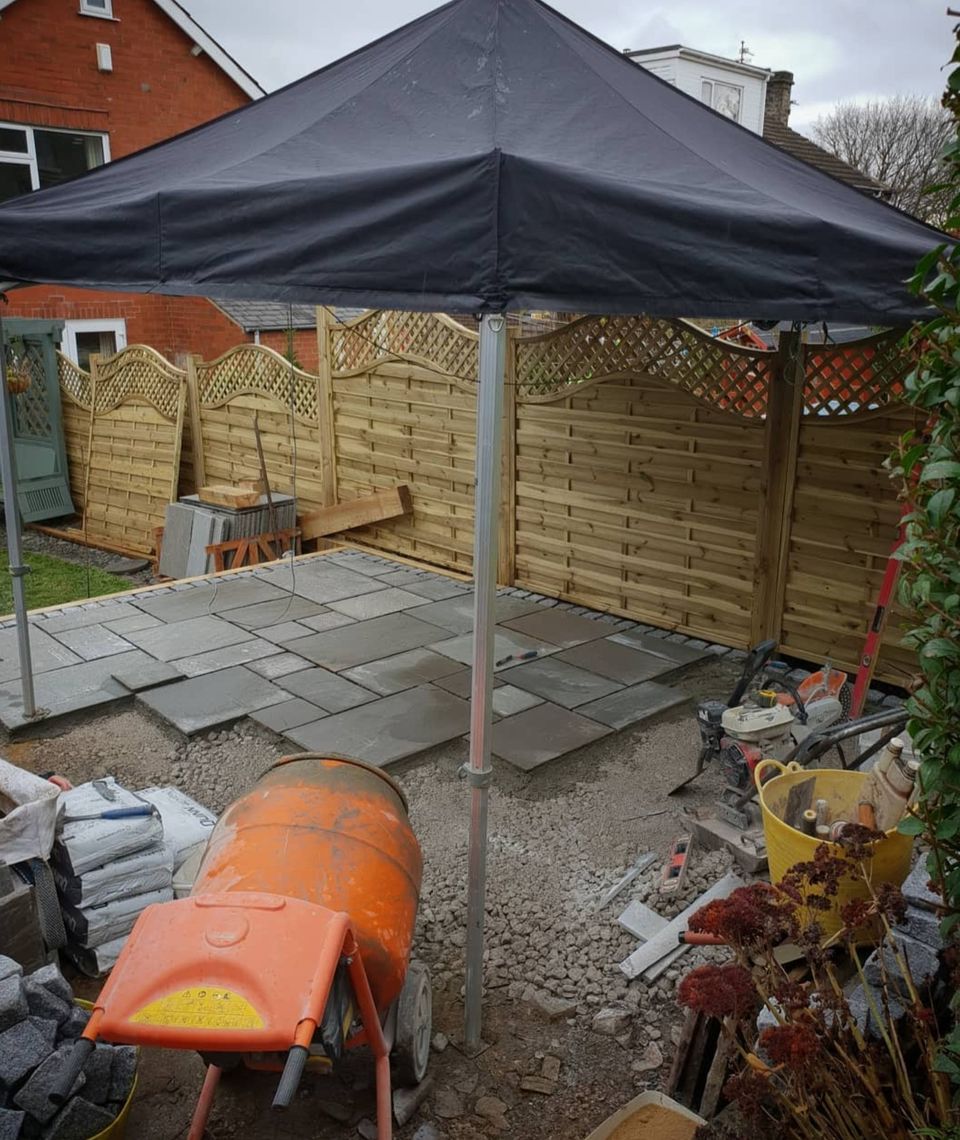 A pop up gazebo over a patio space being built with an orange cement mixer