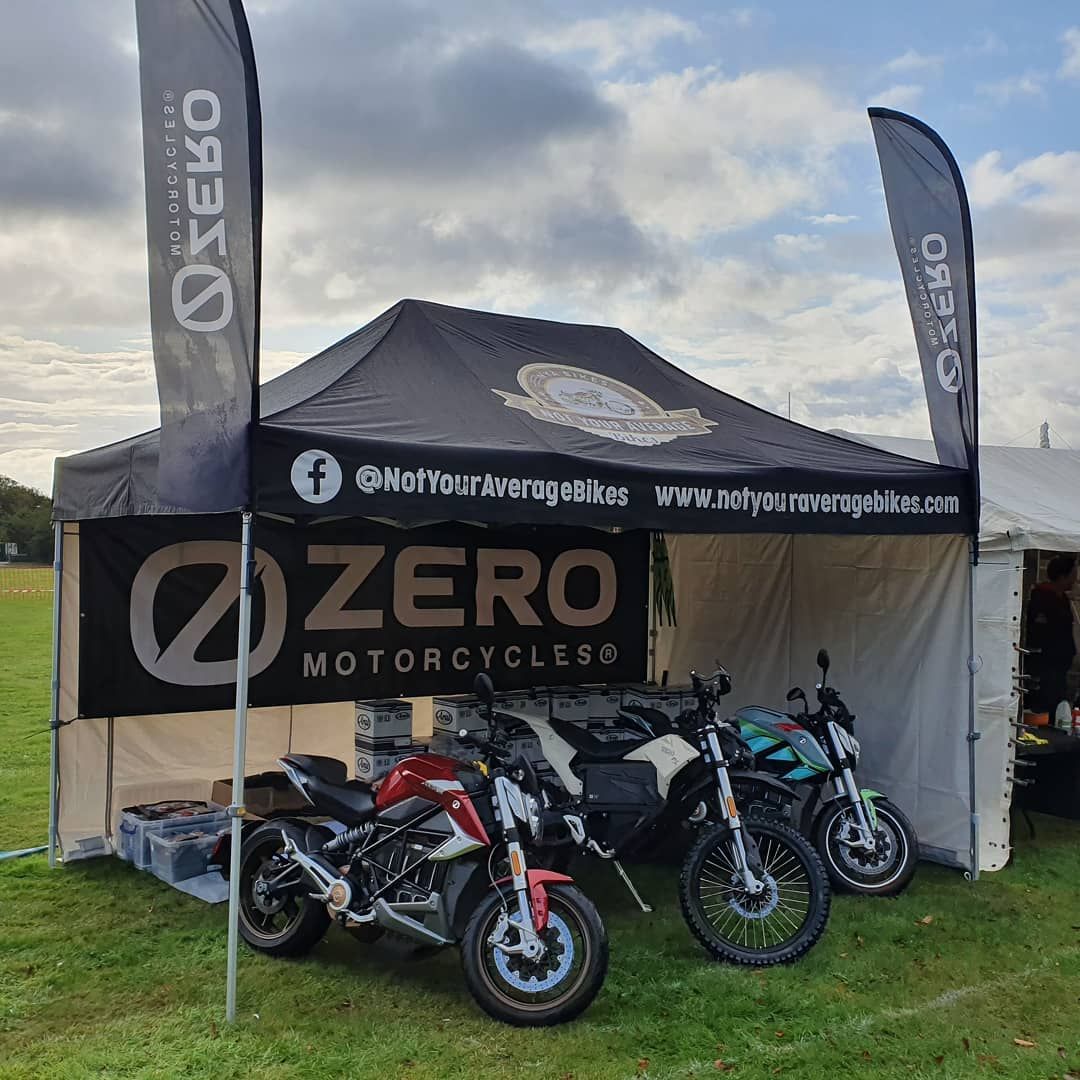 Motorcycles beneath a 3m x 4.5m gazebo with a printed canopy, sidewalls and two feather flags