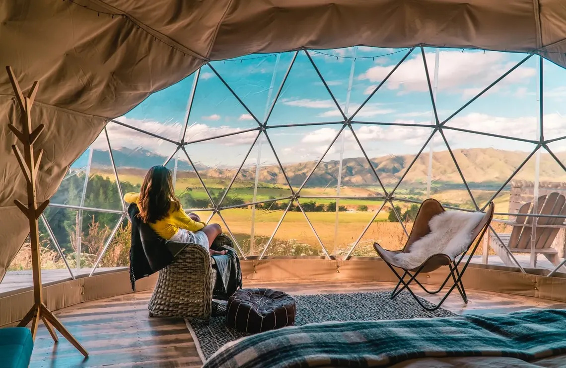 A stunning view through the windows of a geodesic dome. Two people sit inside and look at the vista.