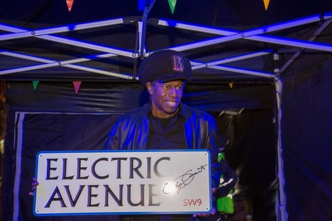 Musician Eddie Grant stands beneath a gazebo holding a sign that reads Electric Avenue