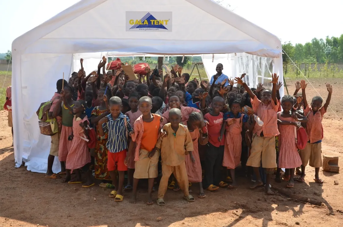 A school of African children stands smiling beneath a marquee