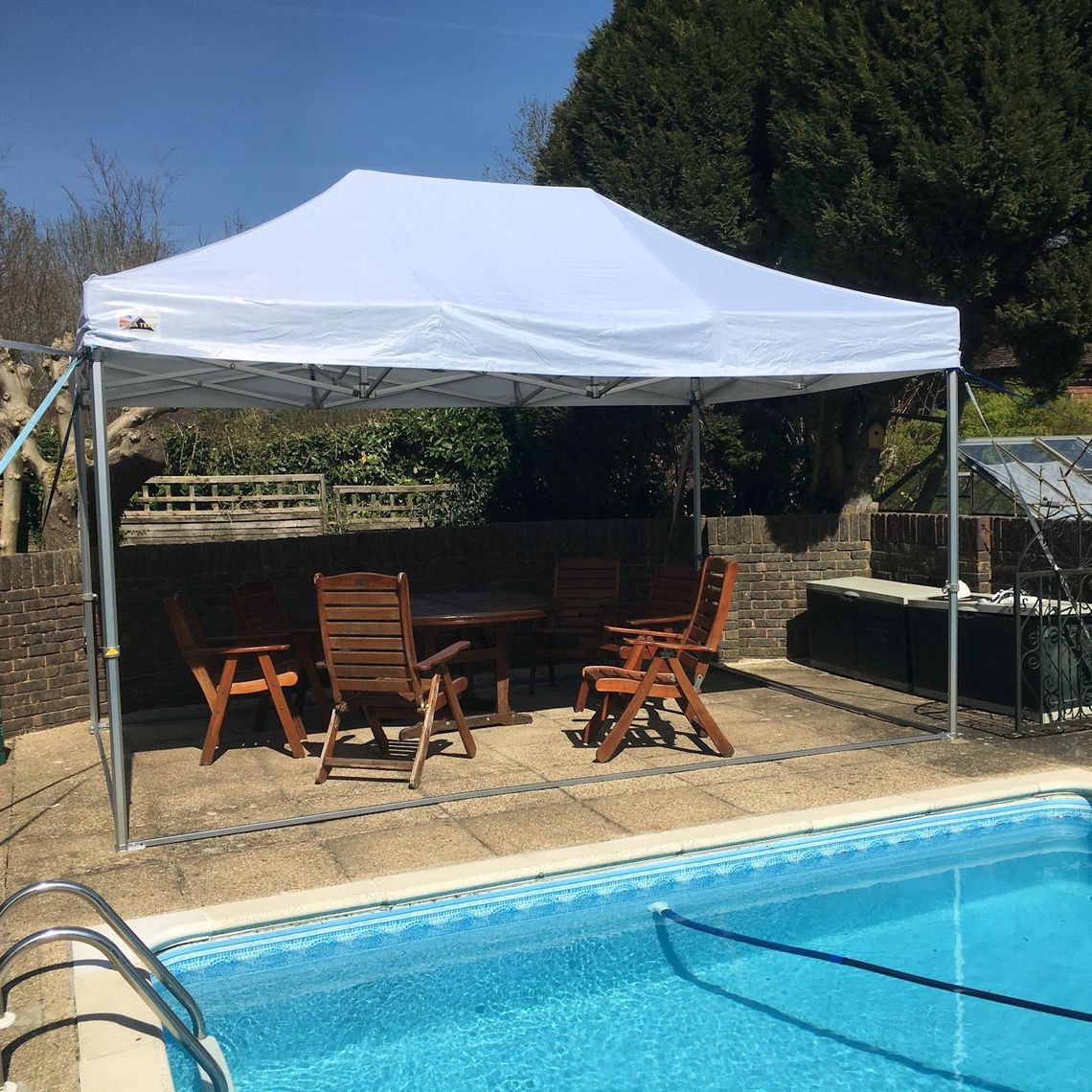 A white garden gazebo over some furniture by a swimming pool